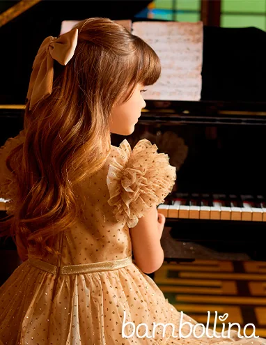 Menina de vestido dourado Bambollina sentada ao piano.