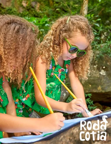 Duas meninas desenhando ao ar livre, vestindo estampa verde da Roda Cotia.